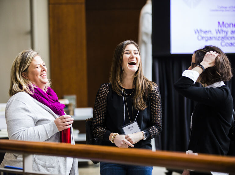Three women laughing together at a conference on campus