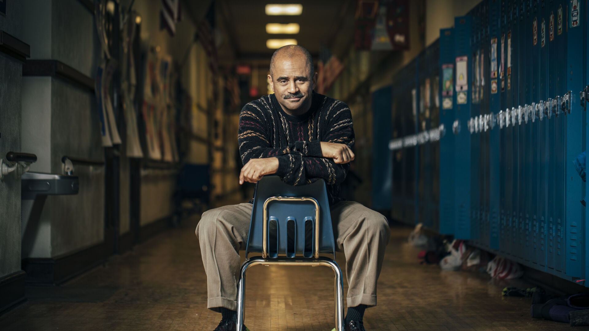 Man sitting on chair in hallway with lockers lining each side of the hallway
